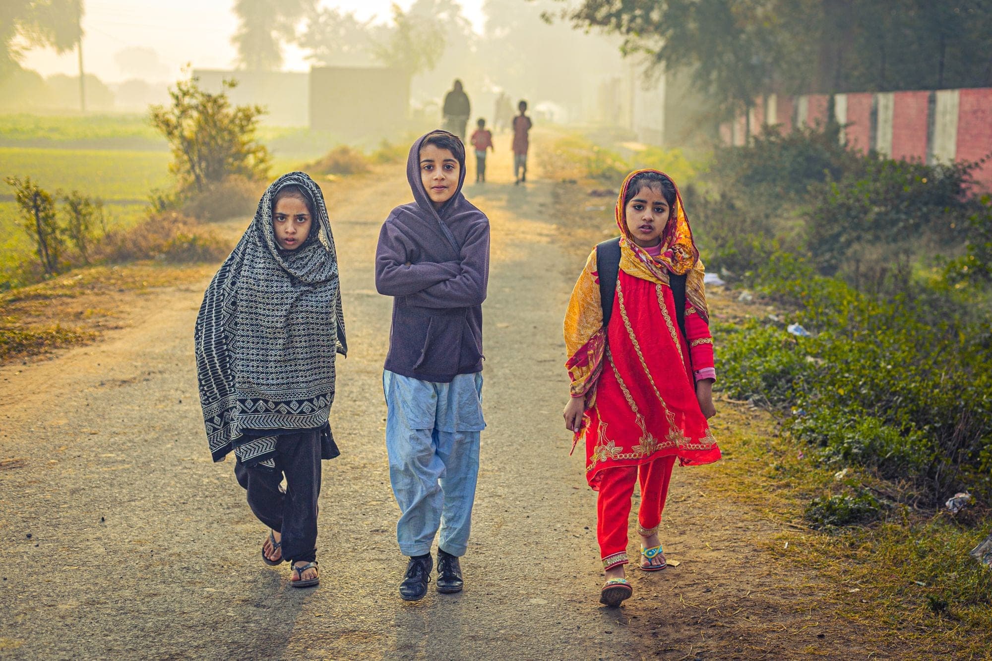 Three children walking together along an unpaved road in morning light